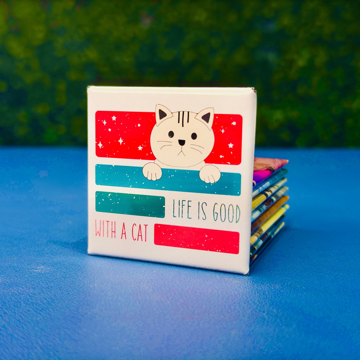 Square cat magnet featuring a sweet cartoon-style tan cat peeking over retro-styled red and teal blocks with the phrase “Life Is Good with a Cat.” A wholesome and cute cat magnet perfect for cat moms, pet lovers, and anyone who appreciates feline-themed decor. Great gift idea for birthdays, stocking stuffers, or thoughtful surprises. Ideal for fridge decor, lockers, or home offices.