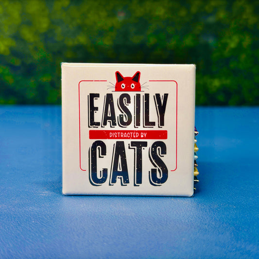 Funny square cat magnet featuring bold vintage-style lettering with the phrase “Easily Distracted by Cats” and a red cartoon cat peeking over the top. A playful and relatable gift for cat lovers, pet parents, and anyone who proudly prioritizes feline distractions. Perfect for fridges, lockers, cubicles, or home office spaces. Great for gifting or daily cat-themed decor.