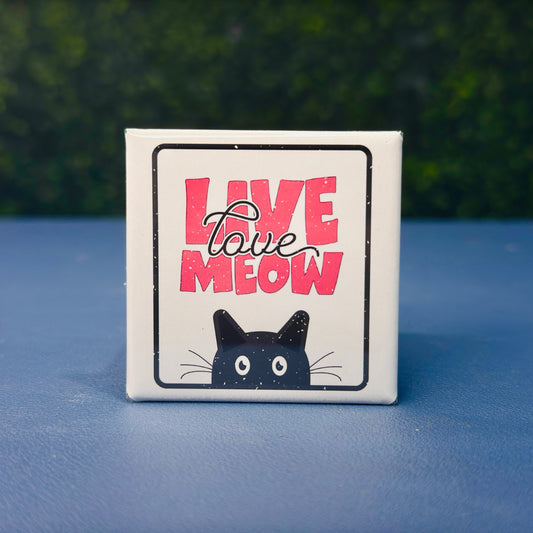 Square cat magnet featuring the phrase “Live Love Meow” in bold pink lettering with a black cartoon cat peeking from the bottom. A cute and funny cat-themed fridge magnet perfect for cat lovers, pet owners, and anyone who loves playful feline decor. Great as a gift for cat moms, stocking stuffer, or whimsical kitchen accessory. Ideal for fridges, lockers, or office magnet boards.