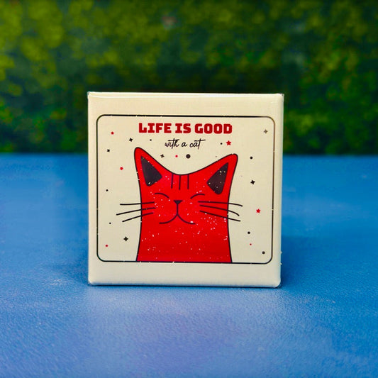 Square magnet with a red cartoon cat smiling under the phrase “Life Is Good With a Cat” in bold red and handwritten script. Surrounded by playful stars, this magnet brings charm and feline joy to fridges, lockers, or desks. A purr-fect gift for cat moms, cat dads, or anyone who knows that life really is better with a kitty around.