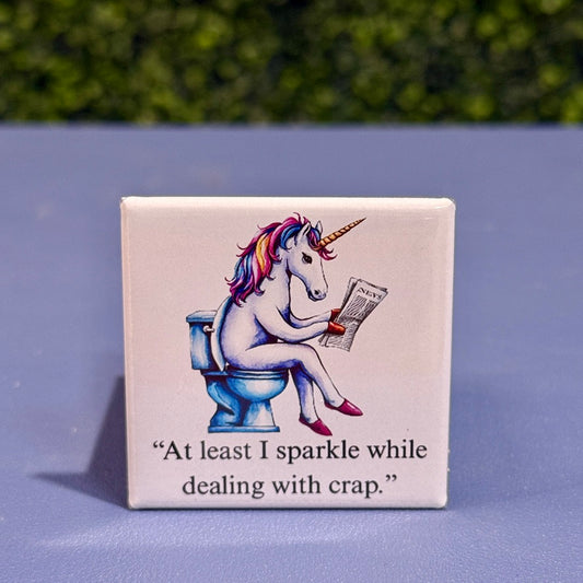 2x2 square funny unicorn magnet featuring a rainbow unicorn on a toilet reading a newspaper with the quote “At least I sparkle while dealing with crap” – adult humor fridge magnet, novelty gag gift for unicorn lovers.