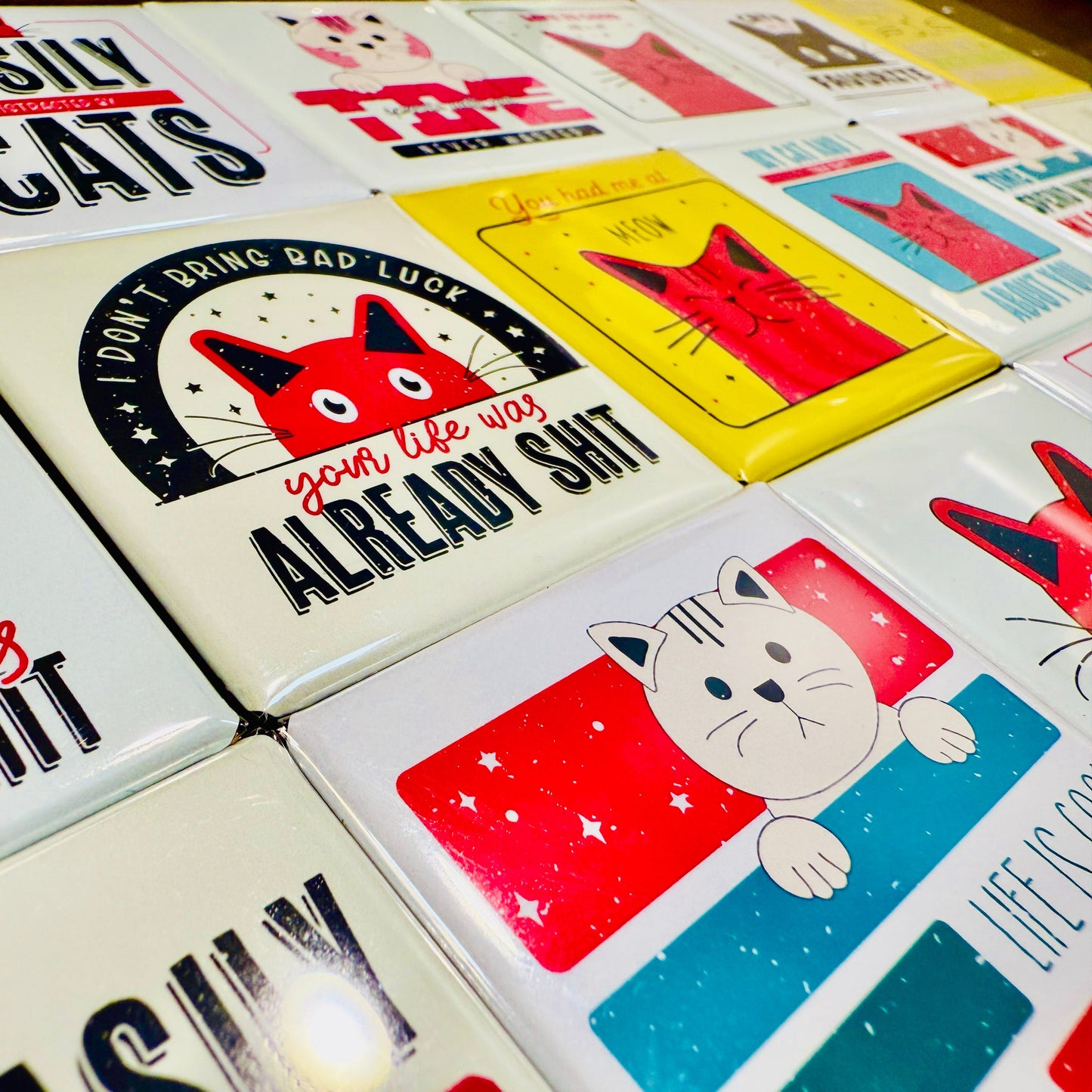 Collection of colorful cat-themed magnets with various designs and text.