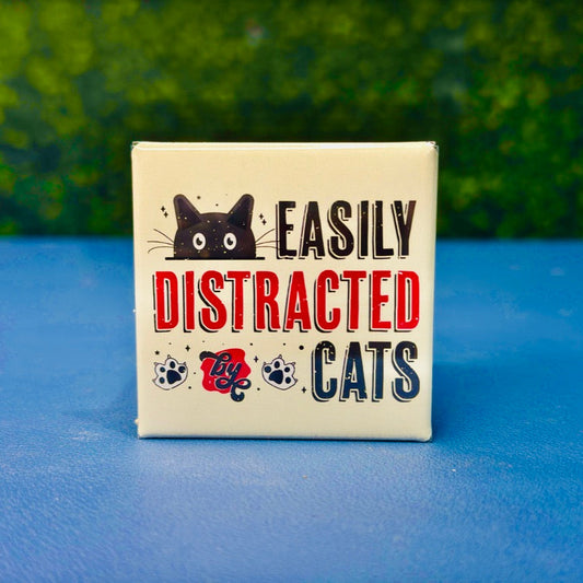 Funny cat magnet featuring a wide-eyed black cartoon cat, paw prints, and bold lettering that reads “Easily Distracted by Cats.” Retro color scheme and distressed design give it vintage charm. Perfect gift for cat moms, pet lovers, or anyone who proudly admits cats steal their focus. Great for fridges, lockers, cubicles, or as a fun addition to your feline-themed decor collection.