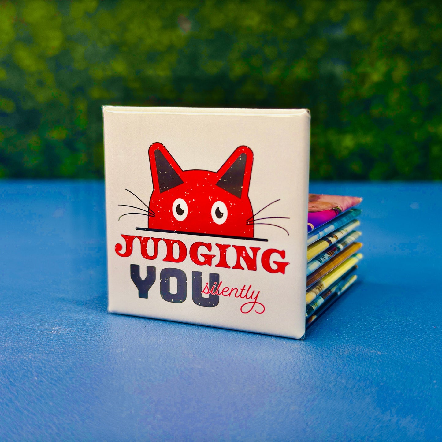 Square cat magnet featuring a red cartoon cat peeking over a ledge with the phrase “Judging You Silently” in bold red, black, and script fonts. A playful and sarcastic gift for cat lovers, introverts, or anyone with a sense of humor about being silently judged by their feline friend. Great for fridges, office boards, lockers, or as a gift for sassy pet owners and cat moms.