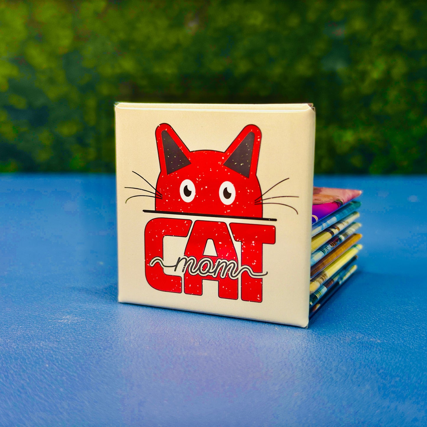 Cute square cat magnet featuring a bold red cartoon cat face peeking over the word “CAT” with the script word “mom” layered on top. Retro-inspired and lightly distressed, this magnet is the perfect gift for cat moms, pet lovers, and anyone who proudly spoils their feline friend. A fun addition to fridges, lockers, or home office boards. Great for birthdays, Mother’s Day, or just because.