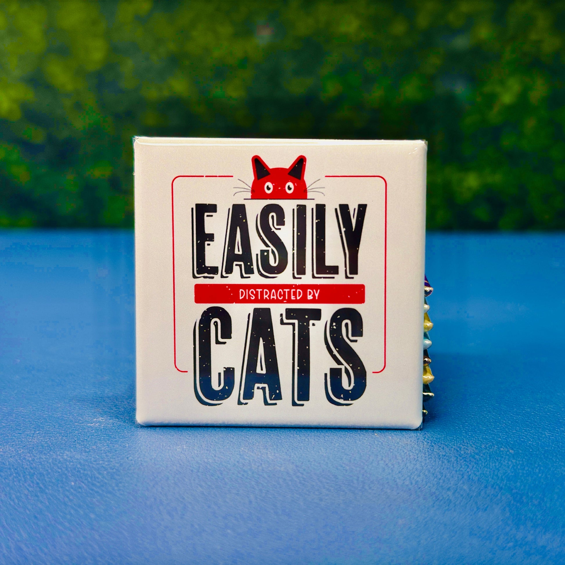 Funny square cat magnet featuring bold vintage-style lettering with the phrase “Easily Distracted by Cats” and a red cartoon cat peeking over the top. A playful and relatable gift for cat lovers, pet parents, and anyone who proudly prioritizes feline distractions. Perfect for fridges, lockers, cubicles, or home office spaces. Great for gifting or daily cat-themed decor.
