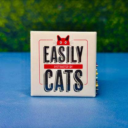 Funny square cat magnet featuring bold vintage-style lettering with the phrase “Easily Distracted by Cats” and a red cartoon cat peeking over the top. A playful and relatable gift for cat lovers, pet parents, and anyone who proudly prioritizes feline distractions. Perfect for fridges, lockers, cubicles, or home office spaces. Great for gifting or daily cat-themed decor.
