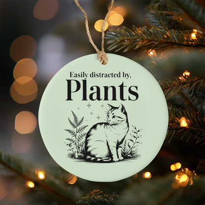 Circular ornament with a cat and plant illustration and text 'Easily distracted by plants' hanging on a Christmas tree.