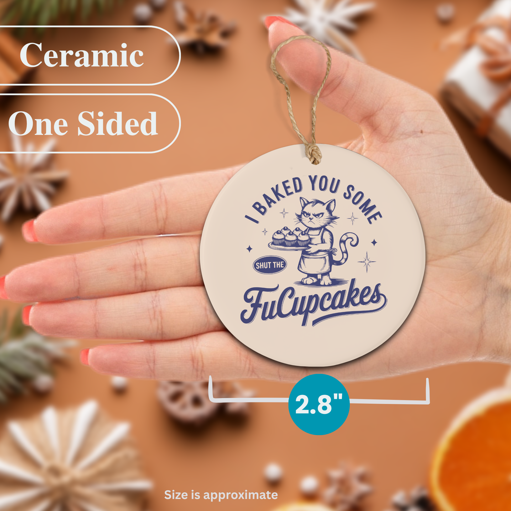 Ceramic ornament with 'I Baked You Some FuCupcakes' text held by a hand, surrounded by decorative items.