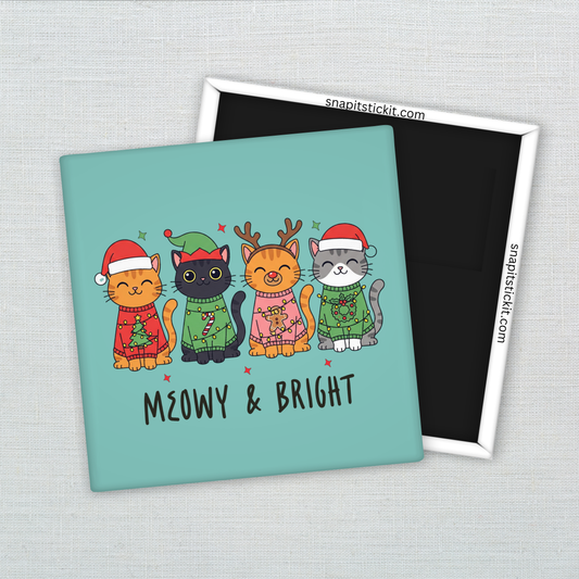 Four illustrated cats wearing festive holiday sweaters, hats, antlers, and scarves, standing in a row on a teal background. Text below reads: “Meowy & Bright.” 2x2 magnet.
