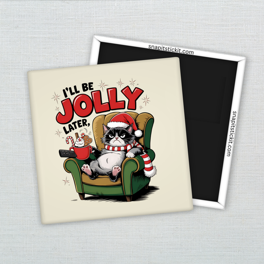 Grumpy black-and-white cat in a Santa hat and striped scarf, sitting in a green chair holding cocoa and cookies. Text: “I’ll Be Jolly Later.” 2x2 magnet.