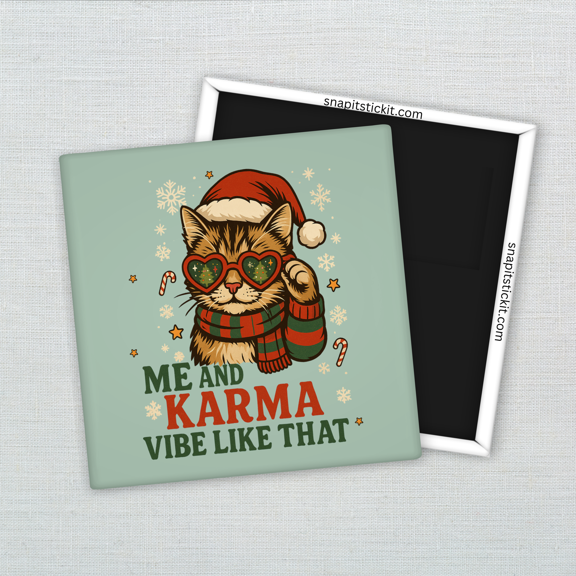 Striped cat in Santa hat and heart-shaped sunglasses with scarf, surrounded by snowflakes and candy canes. Text reads “Me and Karma Vibe Like That.” Funny 2x2 holiday magnet.