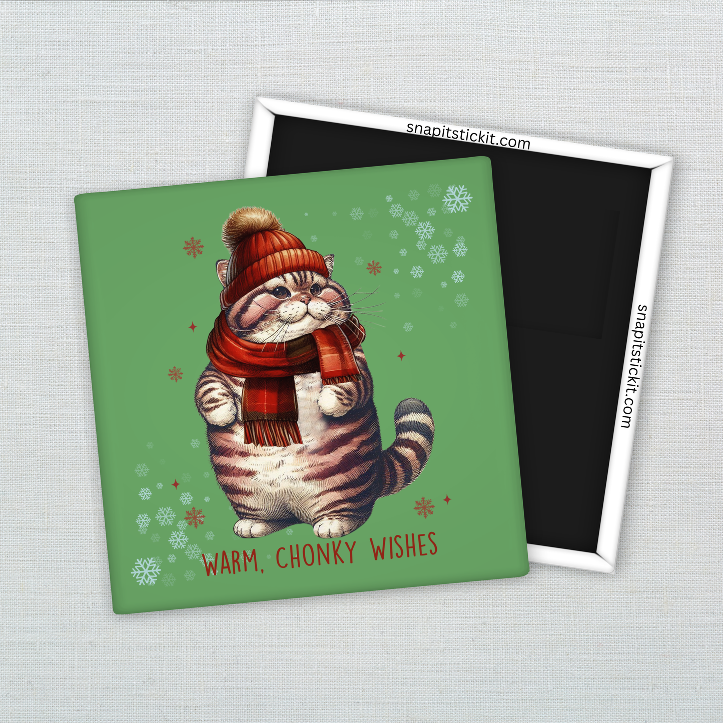 Chubby tabby cat wearing a red scarf and winter hat, surrounded by snowflakes on green background. Text reads “Warm, Chonky Wishes.” Cute 2x2 holiday magnet.