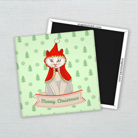 Hairless Sphynx cat wearing a red bonnet, sitting under a “Merry Christmas” banner on a light green background with pine trees. Funny 2x2 holiday magnet.
