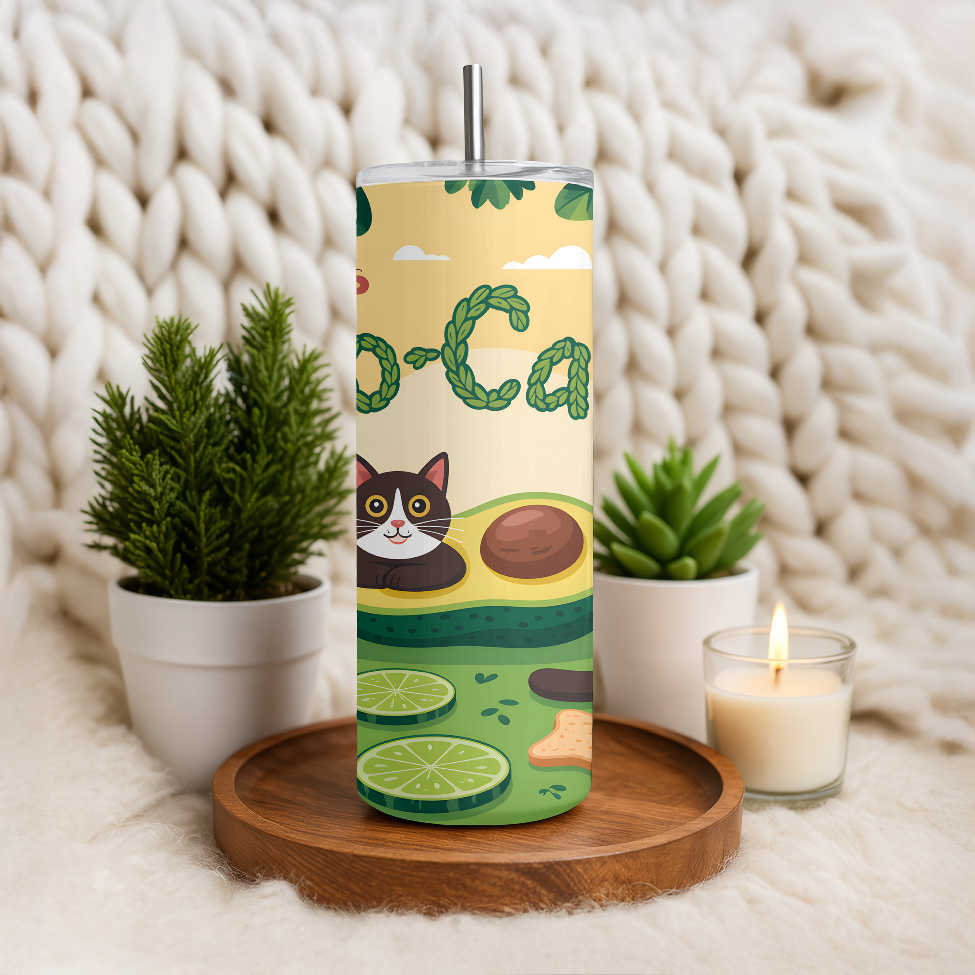 Tumbler with avocado design featuring a cat illustration on a wooden tray with plants and a candle.