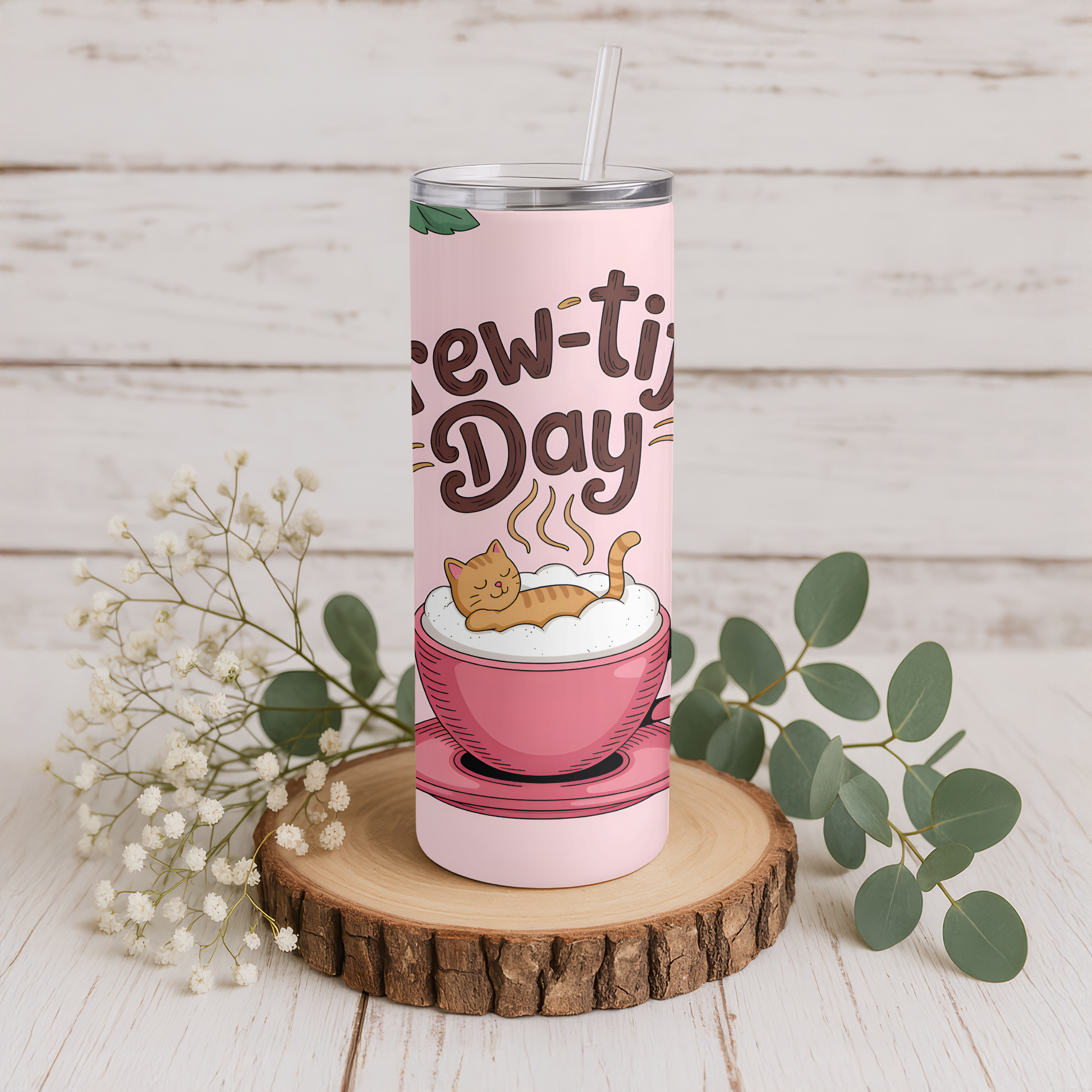 Pink tumbler with a cat design on a wooden surface with greenery.