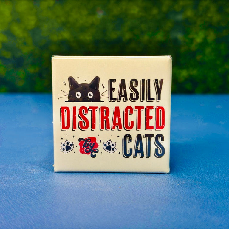 Funny cat magnet featuring a wide-eyed black cartoon cat, paw prints, and bold lettering that reads “Easily Distracted by Cats.” Retro color scheme and distressed design give it vintage charm. Perfect gift for cat moms, pet lovers, or anyone who proudly admits cats steal their focus. Great for fridges, lockers, cubicles, or as a fun addition to your feline-themed decor collection.