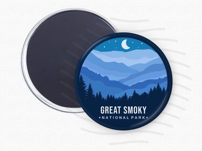 Round magnet of Great Smoky Mountains National Park featuring layered blue mountain ridges under a crescent moon and starry night sky with a silhouette of pine trees in the foreground.