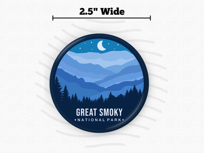 Round magnet of Great Smoky Mountains National Park featuring layered blue mountain ridges under a crescent moon and starry night sky with a silhouette of pine trees in the foreground.