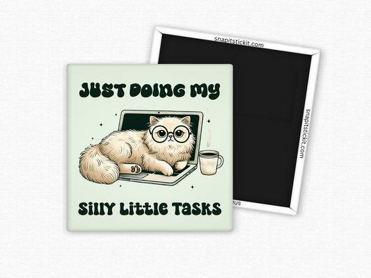 Square magnet featuring a fluffy cat with glasses lounging on a laptop, next to a coffee mug, with the phrase ‘Just Doing My Silly Little Tasks’ in bold playful text.