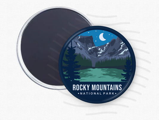 Round magnet of Rocky Mountains National Park featuring snow-capped peaks under a crescent moon, with a green alpine lake and dark pine trees in the foreground