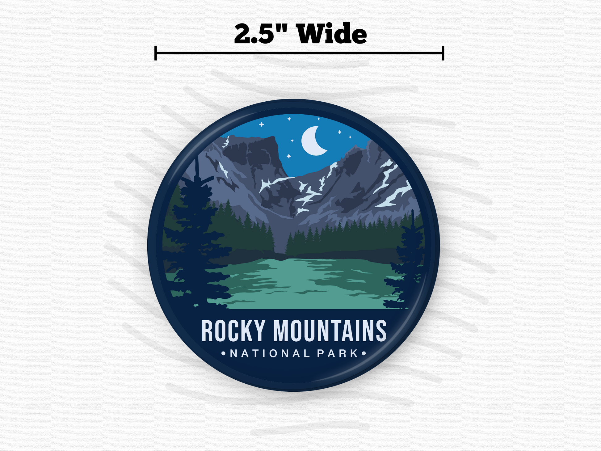 Round magnet of Rocky Mountains National Park featuring snow-capped peaks under a crescent moon, with a green alpine lake and dark pine trees in the foreground
