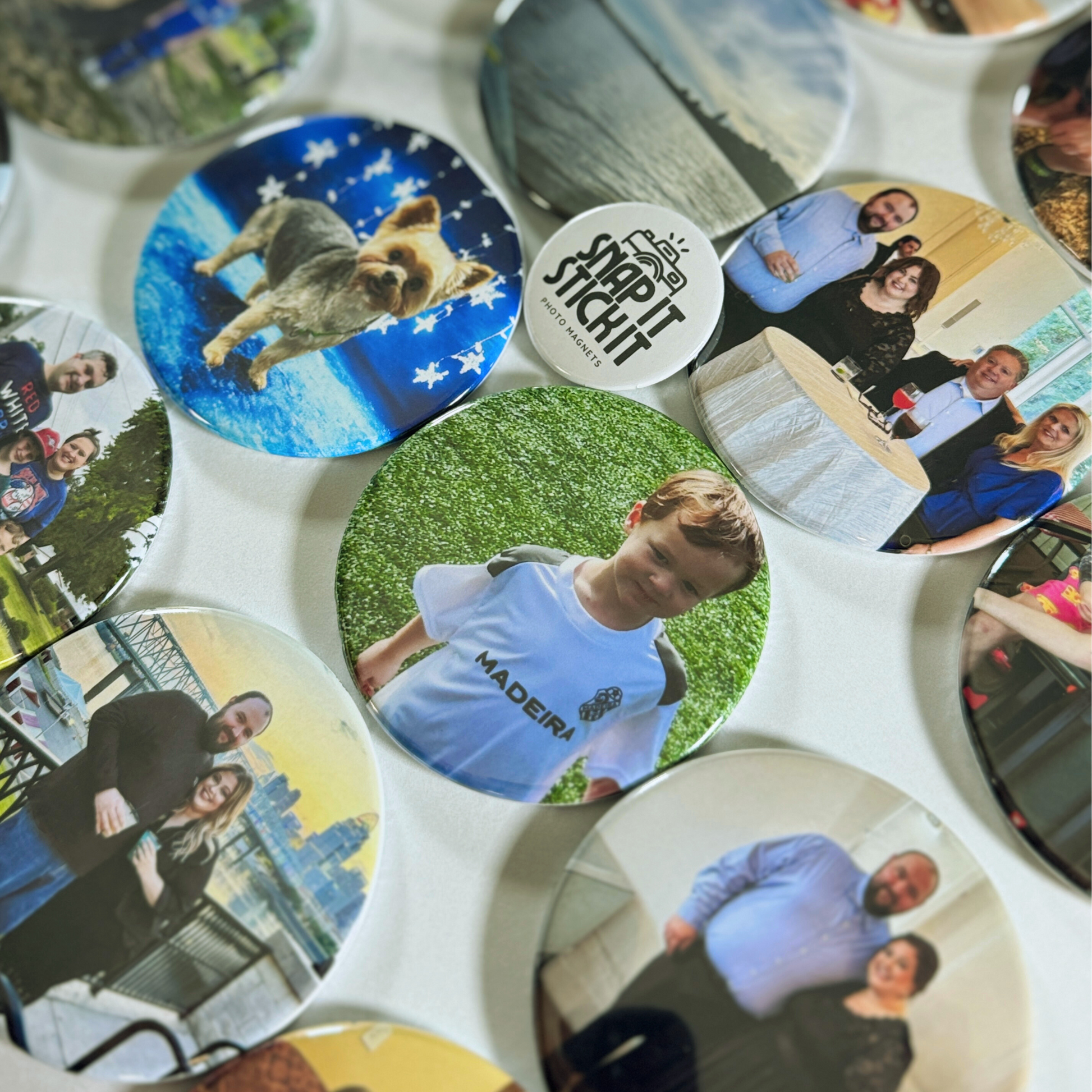 “Collection of custom photo magnets featuring family moments, pets, and nature photos, arranged in a flat lay with the Snap It Stick It logo magnet in the center. Highlights product variety and personalization options.”